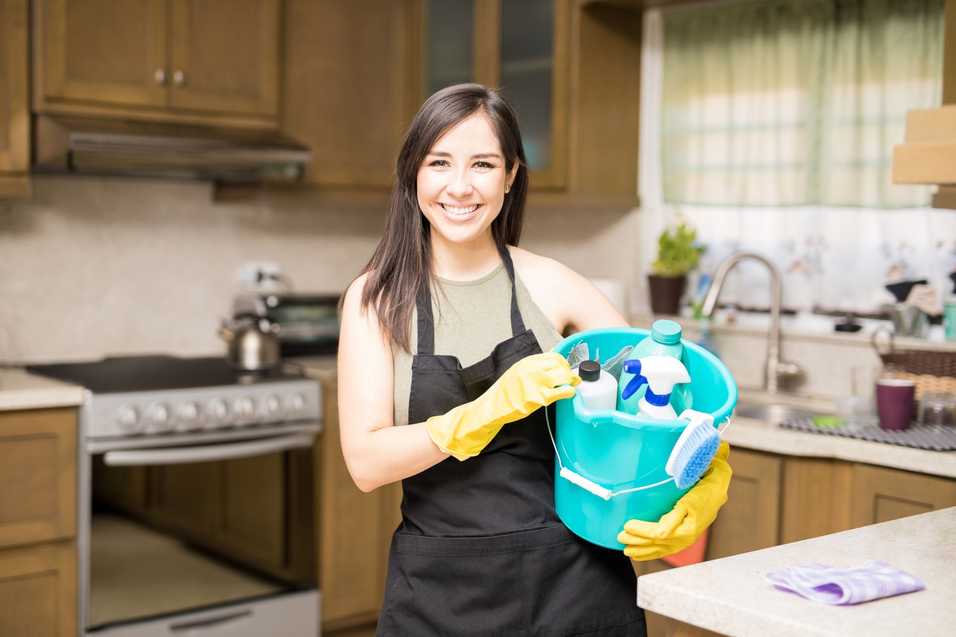 Young woman holding cleaning tools and products in bucket